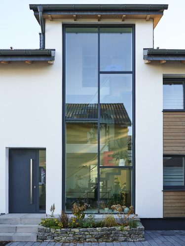 Hinter der Glasfassade des renovierten Hauses ist das Treppenhaus über zwei Etagen zu sehen.