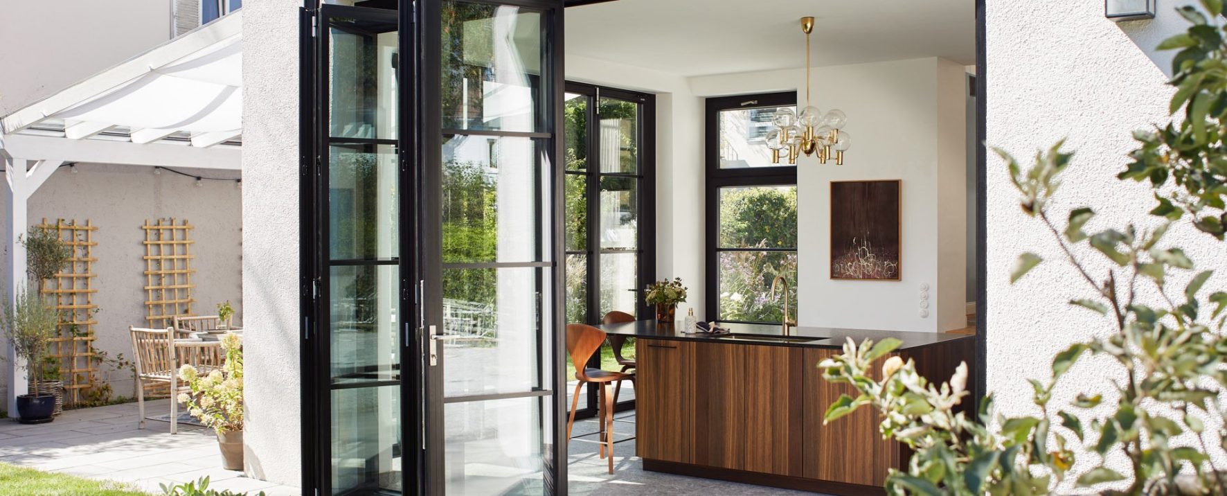 Die 5-teilige Glas-Faltwand im Loftdesign ist halb geöffnet, vom Garten fällt der Blick in die Küche.